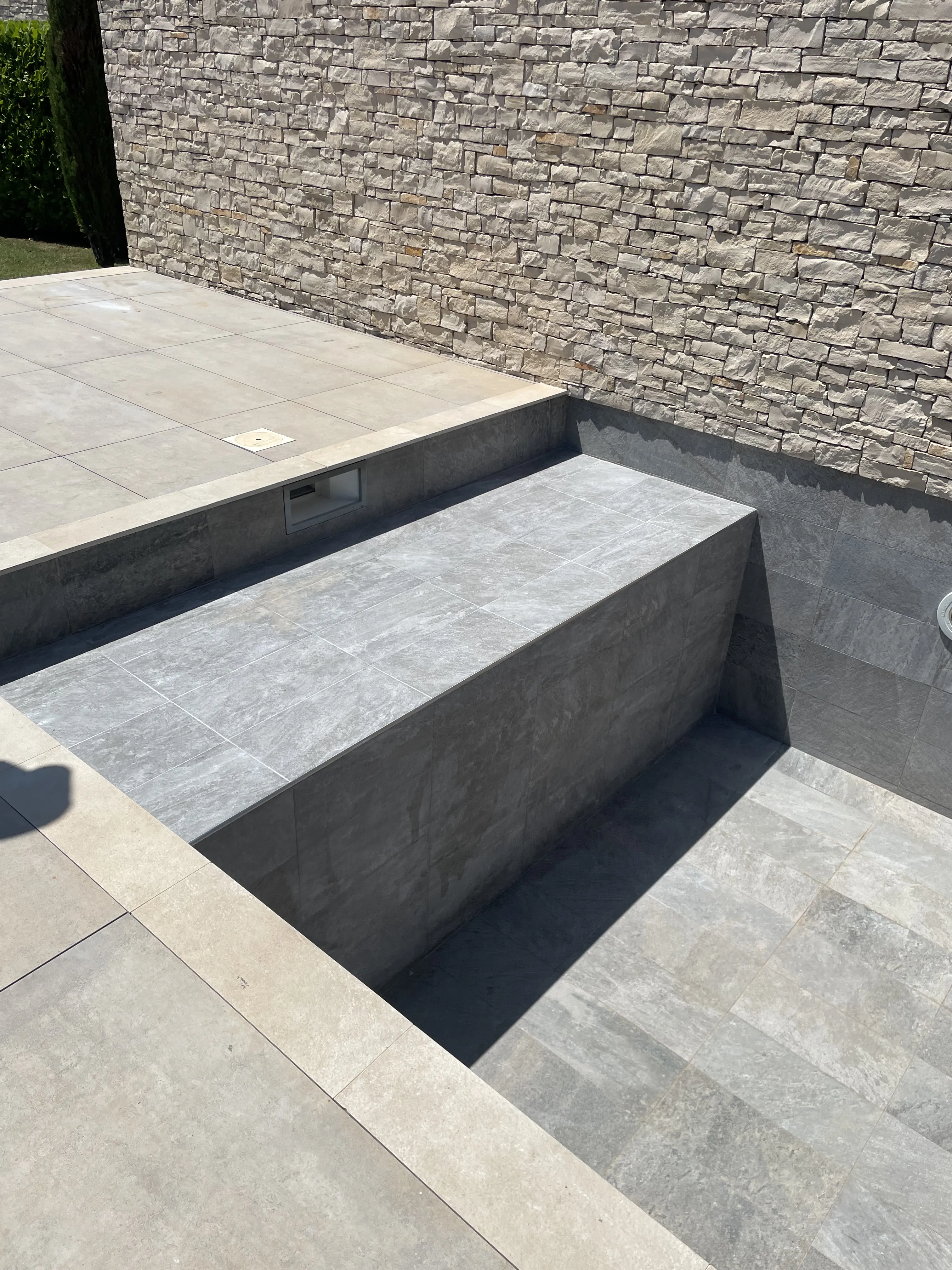 Dettaglio della scala di vasca spa in gres grigio, accanto a muro in pietra